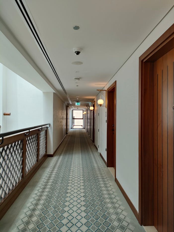 A well-lit hotel corridor featuring wooden doors and elegant carpet, showcasing modern interior design.
