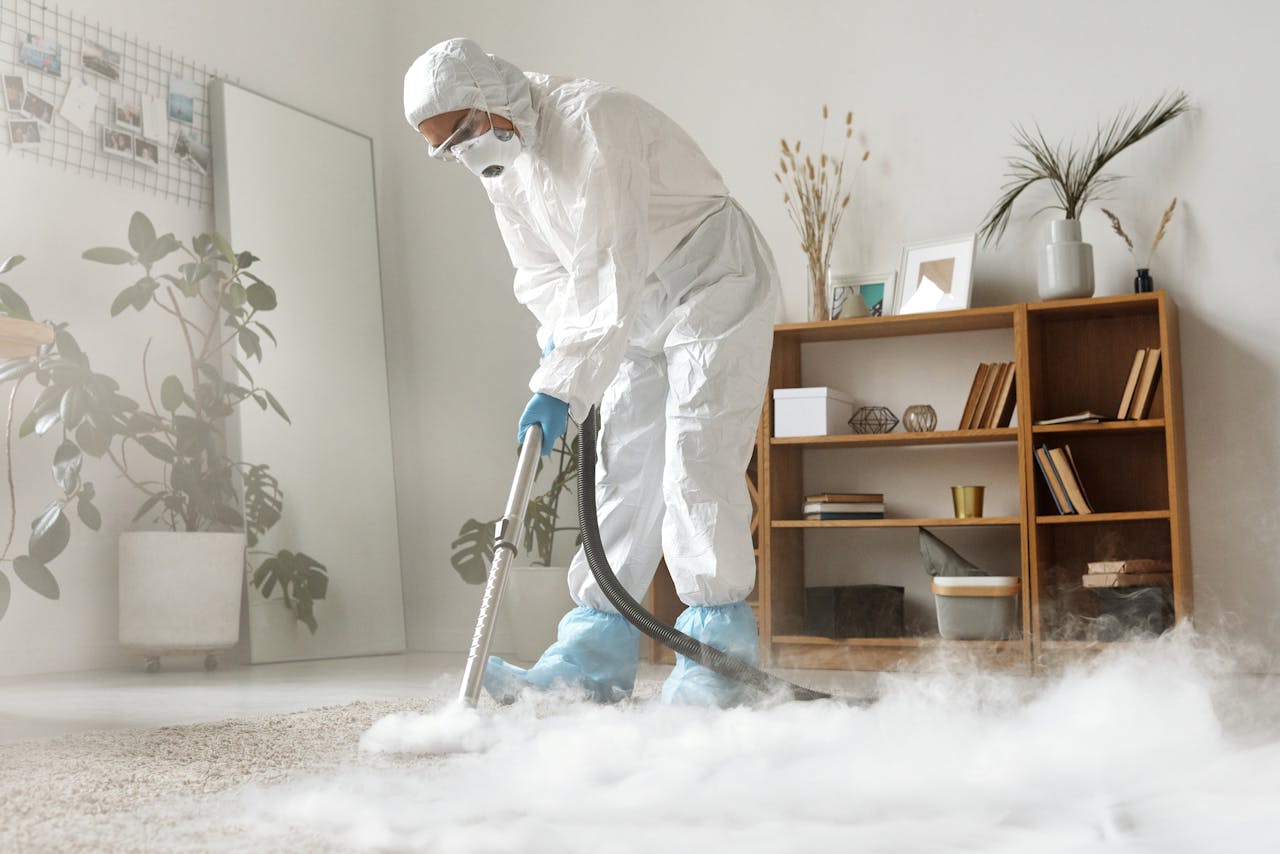 Person in protective suit disinfecting room with fogging device for sanitation.