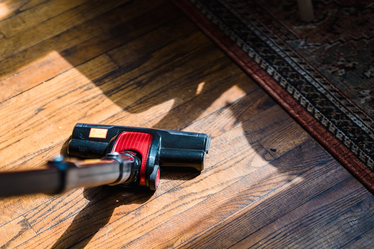 Close-up of a vacuum cleaner on wooden flooring near a patterned rug, showcasing domestic cleaning.